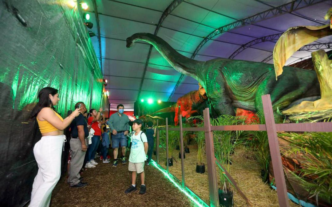 Visitantes posan en la Expo Dinosaurios con un Brachiosaurus a sus espaldas, la ciudad de Tizimín.